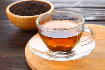 Hot black tea in a glass cup and dry tea on a wooden table.