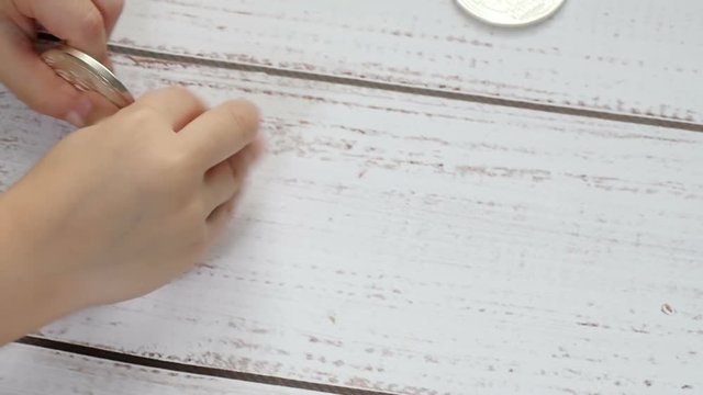 The child's hands are playing with bitcoin coins on a wooden table. The child plays with a crypto currency. Close up