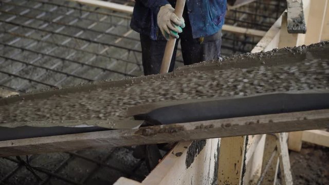 laborer is controlling pouring concrete mixture from pump onto reinforcement cage, holding spade and nudging