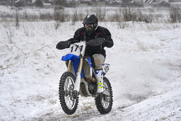 Fototapeta na wymiar Sportsman racer man fulfills a fast ride on a motorcycle on the road extreme. The race track is very uneven. Cloudy winter day with a snowstorm.