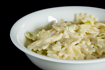 A bowl of bow tie pasta salad on a black background.
