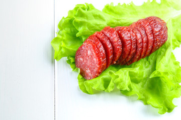 Smoked sausage, salami chopped in slices on a salad on a wooden circular cutting board on a white table.