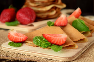 Golden crepes with fresh strawberries and mint on a wooden board 