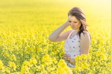 Beautiful young woman with flower in summer meadow looking down. Beautiful girl eyes closed in yellow flowers field infinite horizon. Sunny sun sunshine and authentic lifestyle in windy weather hair