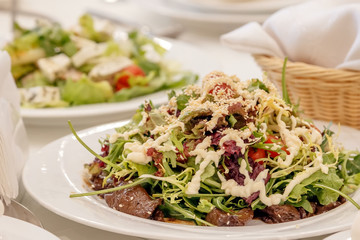 Salad from the mix of Italian herbs (iceberg, breeze, mung beans, arugula) and sun dried tomatoes on a white plate on a dark surface. Italian food. Vegetarian, vegan concept.