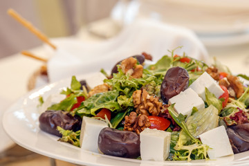 Salad from the mix of Italian herbs (iceberg, breeze, mung beans, arugula) and sun dried tomatoes on a white plate on a dark surface. Italian food. Vegetarian, vegan concept.