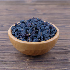 Raisins in a wooden bowl on a wooden background. Side view.