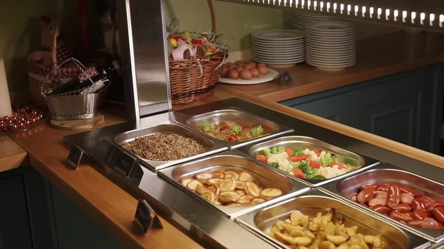 close up shot of the buffet in the hotel, in the containers with Podogev are fried cutlets, steamed vegetables, potatoes, scrambled eggs, fried sausages, buckwheat and sour cream