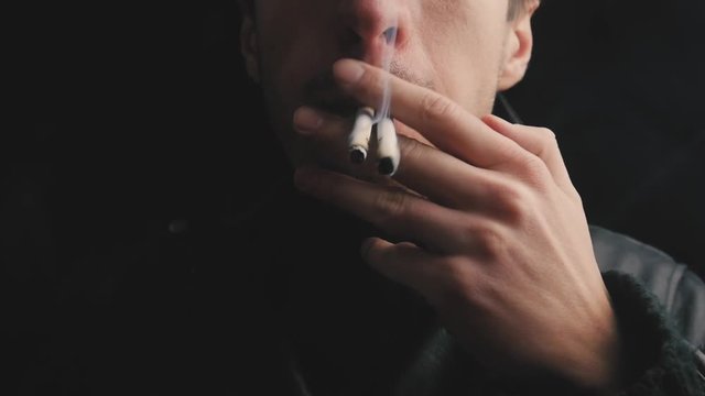 close-up of young man smokes two cigarettes at a time.