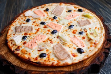 Close up of fresh baked mediterranean fish pizza with salmon, tuna and olives, delicious Italian cuisine