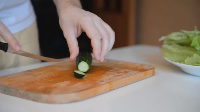 woman is cutting a cucumber with a knife on a wooden board.