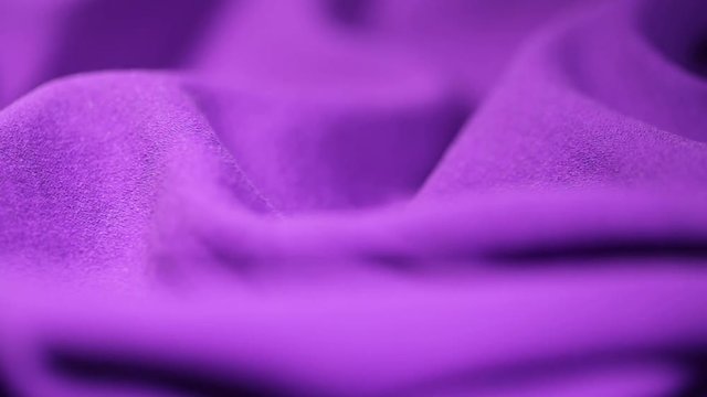 Closeup view of smooth wavy purple cloth rotating fast. Real viscose and polyester synthetic fabric texture.