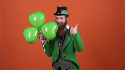 Young man leprechaun celebrating saint patrick's day isolated on orange wall walking with clover-shaped balloons backwards shots