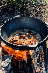 Cooking pilaf in a large boiler with a strong flow on an open fire outdoors on a Sunny summer day . Close up.