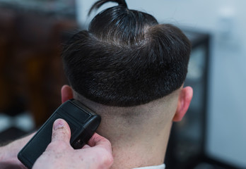 The hands of young barber making haircut to attractive man in barbershop
