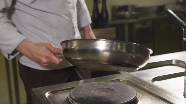 close up shot of a professional chef hands, a man is preparing in the kitchen, he warms up the olive oil in a frying pan, which stands at the plate