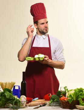 Chef in burgundy uniform holds eggs. Kitchenware and food concept.