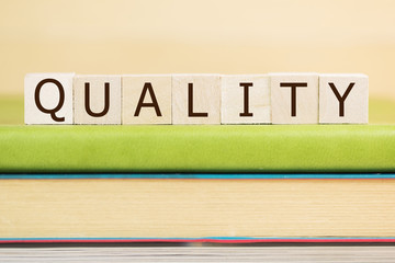 Quality word built with letter cubes on green book