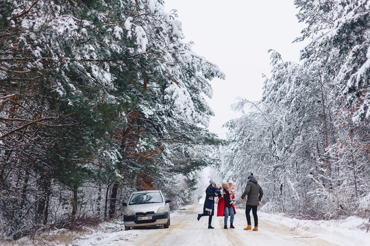 fun company with a little baby on a snowy road under winter pine trees