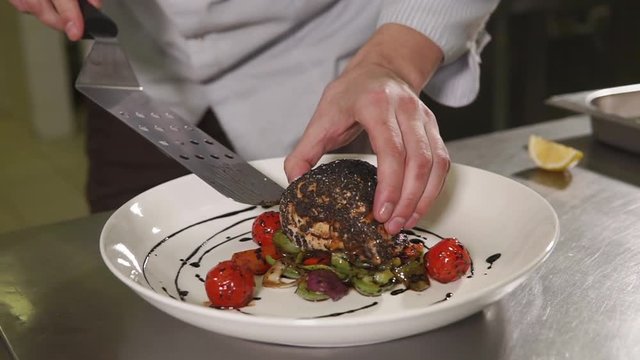 close up shot of the man's hands, the person puts a piece of trout on a plate with fried vegetables in oil, he cooked a delicious dinner for his wife