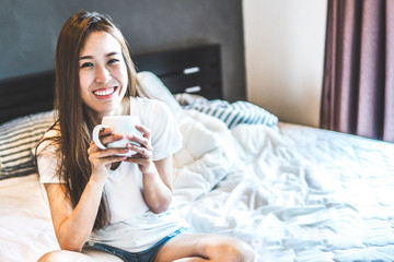 Young woman sit in the bed smiling and drinking hot coffee in the morning.