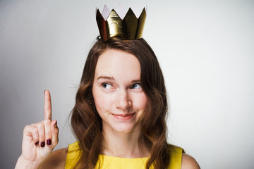 a cute young girl in a yellow dress lifted her index finger up, a golden crown on her head, an idea...