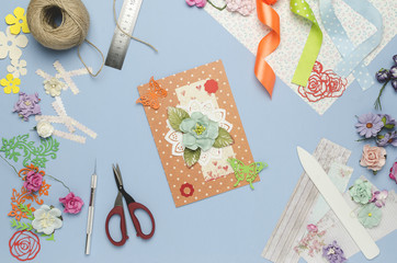 Homemade greeting card made of paper flowers. Scrapbooking, creative mess. Top view, blue background