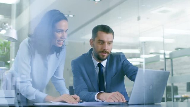 In the Office Female Manager Consults Businessman sitting at His Desk Working on a Laptop, They Succeed in Finishing the Project and High-Five Each Other.  Shot on RED EPIC-W 8K Helium Cinema Camera.