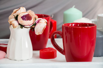 A vase with flowers and a red cup on a white tray