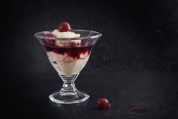 dessert glass with semolina pudding, cherries and fruit sauce on a dark slate background, copy space