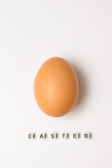 Chicken egg of light brown color on a white background with an Easter inscription from cubes