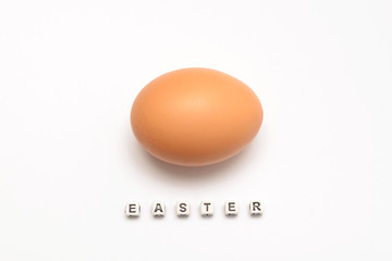 Chicken egg of light brown color on a white background with an Easter inscription from cubes