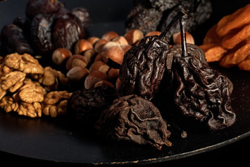 dried pear, prunes, dried apricots on a black plate and background, selective focus. Low key.