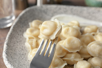 Fork with tasty meat dumpling on plate, closeup