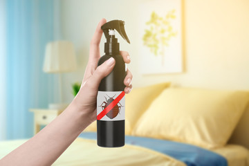 Woman holding bottle of anti bed bug detergent in bedroom