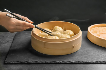 Woman cooking tasty baozi dumplings in bamboo steamer on table