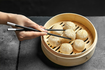 Woman cooking tasty baozi dumplings in bamboo steamer on table