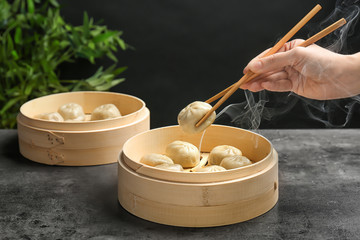 Woman with tasty baozi dumplings in bamboo steamer on table