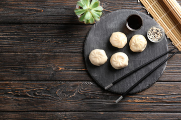 Slate plate with tasty baozi dumplings, sesame and soy sauce on table