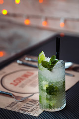 Mojito cocktail with lime and mint in highball glass on a grey table. Blurred LED lights on background. Copy Space