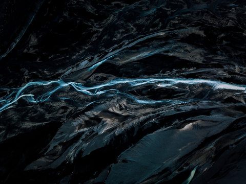 Aerial of an abstract blue river in Iceland in a contrast black sand beach riverbed