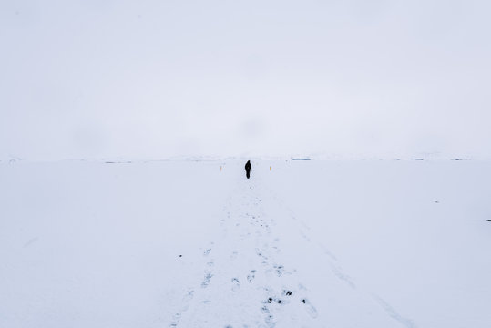 Lone person wandering through a white snowstorm with tracks of footsteps in the foreground 
