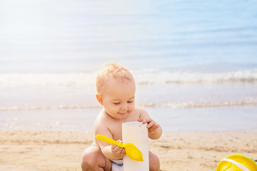 Cute  baby playng in the sand with yellow scoop in summer day at the beach