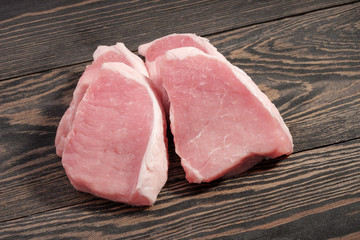 Fresh raw pork steaks on a dark wooden background.