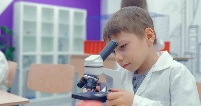Little boy is looking through a microscope in a classroom