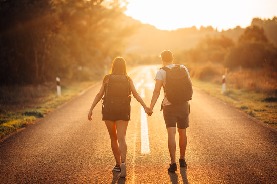 Young Backpacking Adventurous Couple Hitchhiking On The Road.Adventure Of Life.Travel Lifestyle.Low Budget Traveling.Adventurous Active Vacations.Hitchhiking Tourism Concept.Backpackers Together