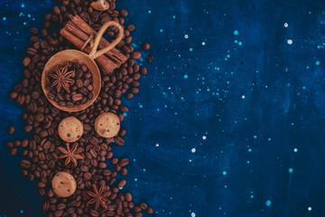 Scattered coffee beans with handmaiden wooden scoop, cinnamon, anise stars and cookies on a dark background. Header or title image with copy space.
