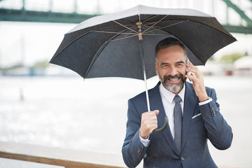 Business man on a rainy day, chatting with a colleague and holding an umbrella