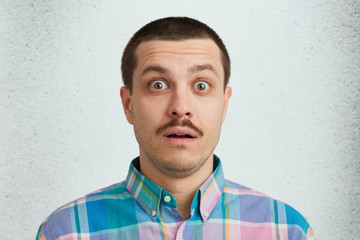 Portrait of unshaved surprised astonished hesitant male with dark warm eyes and mustaches wearing...