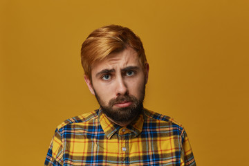 Disappointed unshaven male feels upset. Feel lonliness and sad. Has regretful expression. Dyed blonde gold hair. Isolated over studio yellow background.